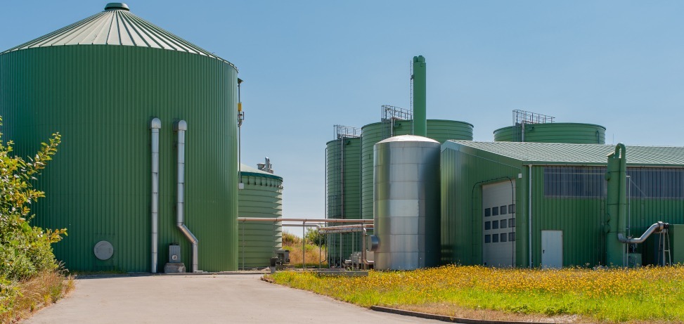 Biomass energy plant with green anaerobic digester tanks and storage silos under a clear sky