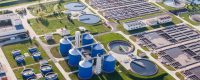 Aerial view of a water treatment plant with blue digester tanks and circular sedimentation basins