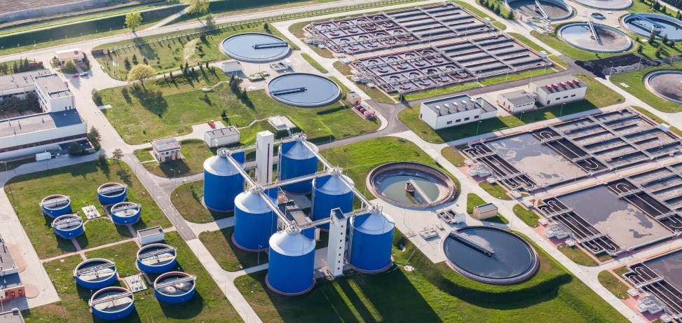 Aerial view of a water treatment plant with blue digester tanks and circular sedimentation basins